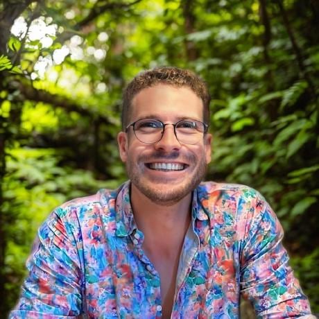 Daniel Larkin, smiling, in dense New Zealand rainforest wearing a bright floral shirt.